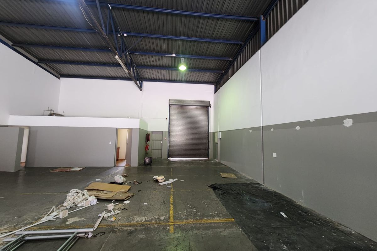 Spacious industrial warehouse unit featuring high ceilings with exposed steel trusses, a large roller shutter door, and durable concrete flooring.