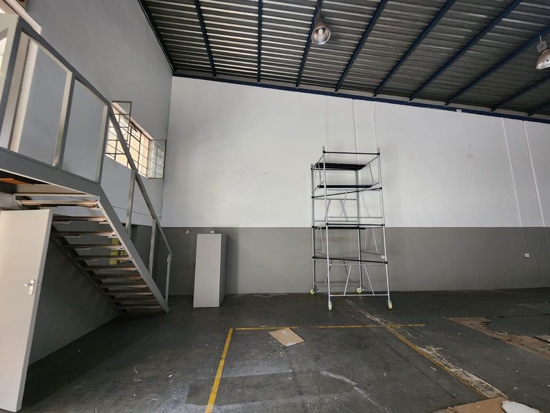 Spacious industrial utility area featuring high ceilings, exposed steel roof structure, concrete flooring, and a built-in metal staircase leading to a mezzanine level.