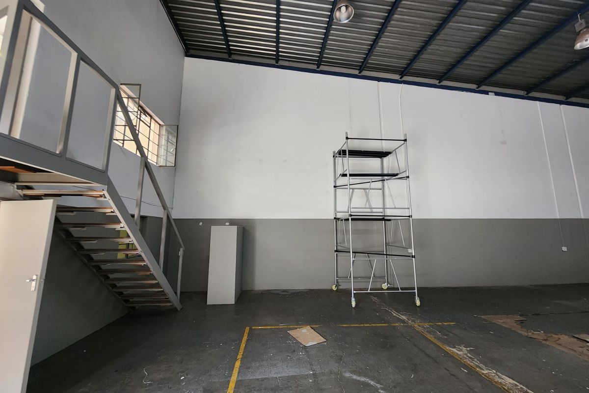 Spacious industrial utility area featuring high ceilings, exposed steel roof structure, concrete flooring, and a built-in metal staircase leading to a mezzanine level.