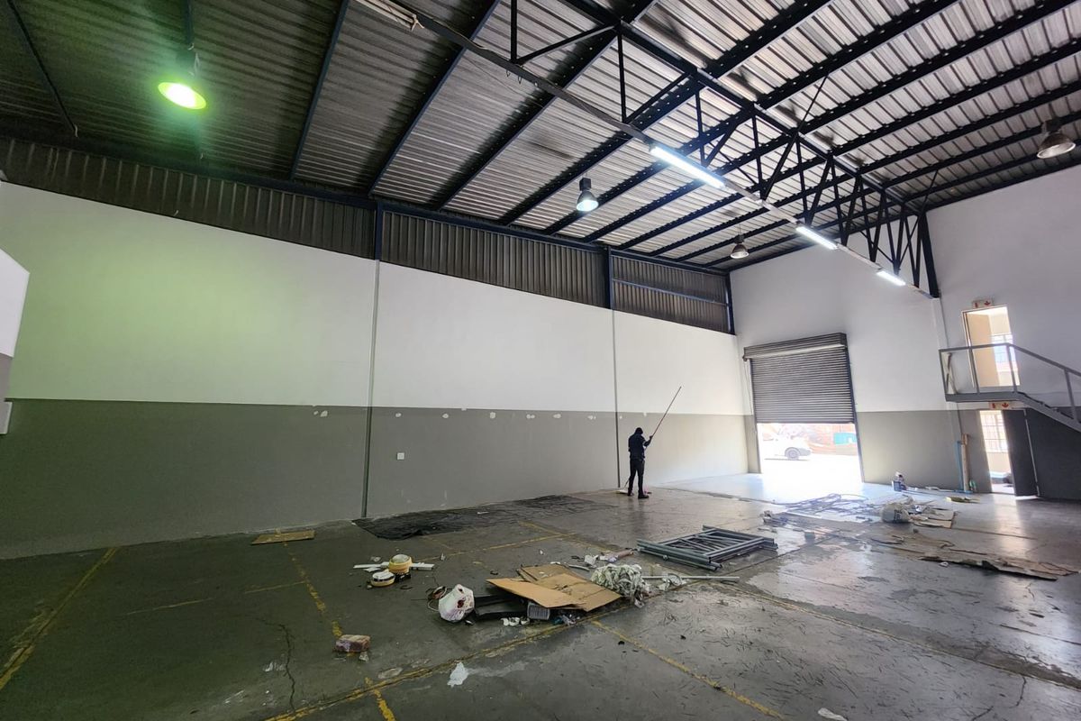 Spacious industrial warehouse unit featuring high ceilings with exposed steel trusses, concrete flooring, and a large roller shutter door for easy access.