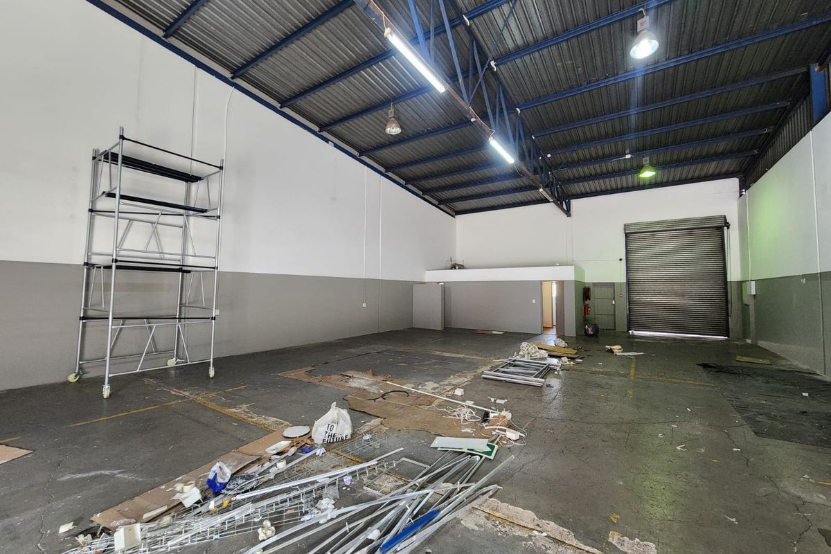 Spacious industrial warehouse unit featuring high ceilings with exposed steel trusses, concrete flooring, and a large roller shutter door for easy access.
