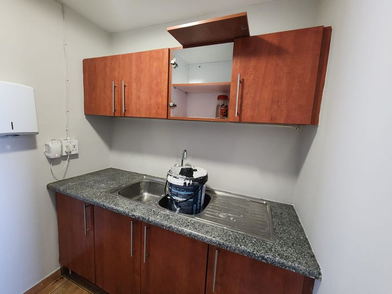 A functional scullery area featuring laminate cabinetry, a granite countertop, and a stainless steel sink, currently requiring minor repairs to the cabinetry.
