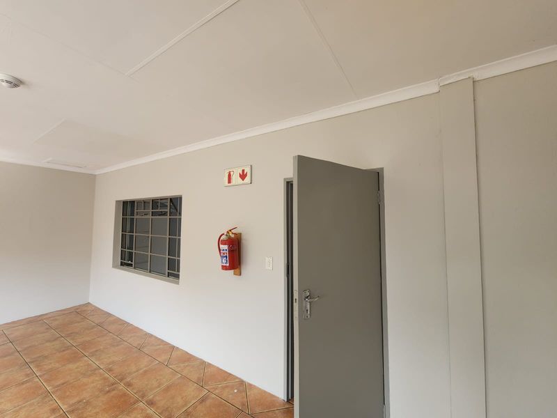 A clean, functional utility space featuring tiled flooring, a secure window with bars, and wall-mounted fire safety equipment.