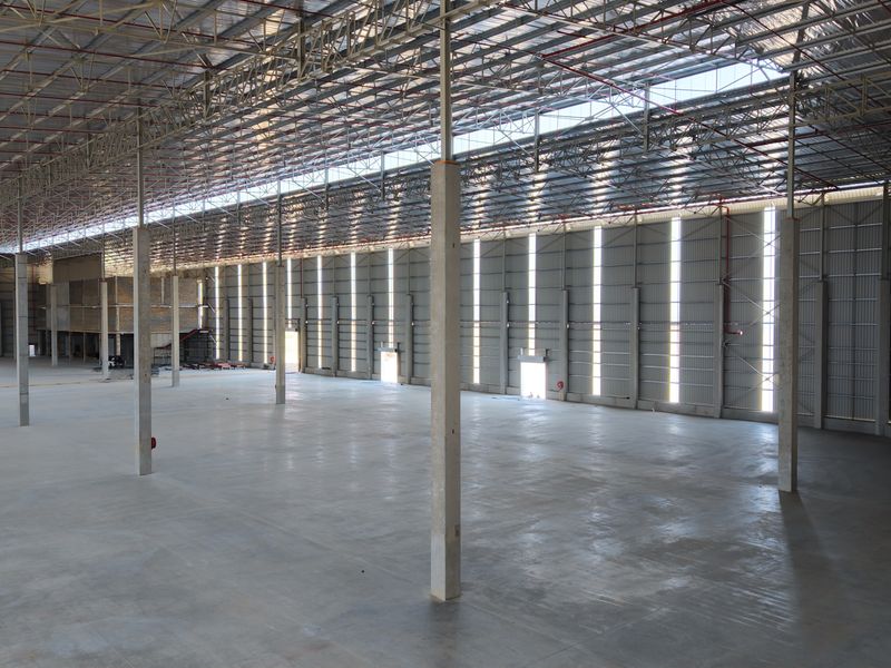A spacious, modern industrial warehouse featuring high ceilings with exposed steel trusses, polished concrete flooring, and integrated fire sprinkler systems.