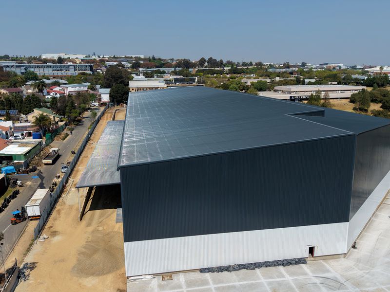 Aerial view of a large industrial warehouse facility featuring metal cladding, a concrete apron, and rooftop solar panels in an established commercial area.