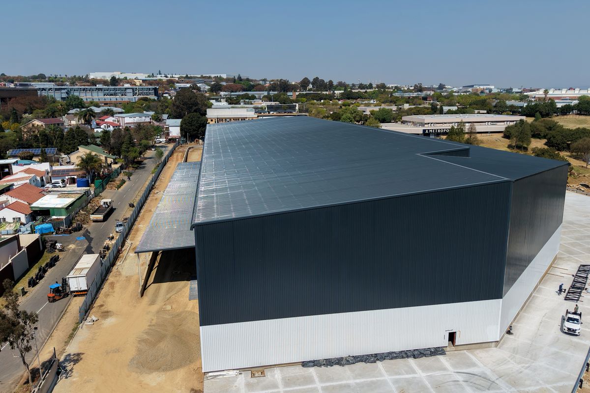 Aerial view of a large industrial warehouse facility featuring metal cladding, a concrete apron, and rooftop solar panels in an established commercial area.