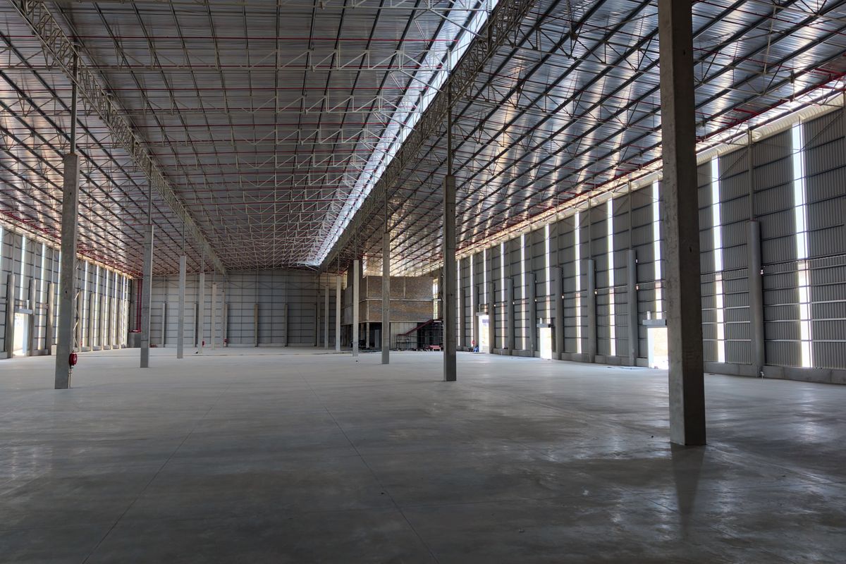Spacious industrial warehouse featuring high ceilings, concrete flooring, steel truss roofing, and integrated fire sprinkler systems, suitable for large-scale storage or manufacturing operations.