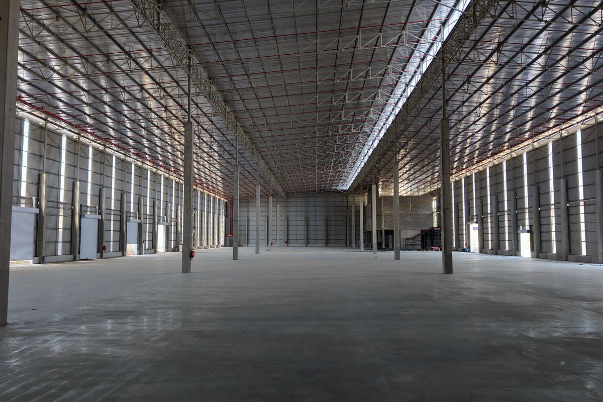 A large, open-plan industrial warehouse space featuring high ceilings, concrete flooring, and robust steel structural elements, suitable for logistics or manufacturing operations.
