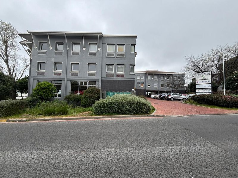 Front exterior view of a multi-story office building featuring a paved driveway, professional signage, and established garden landscaping.
