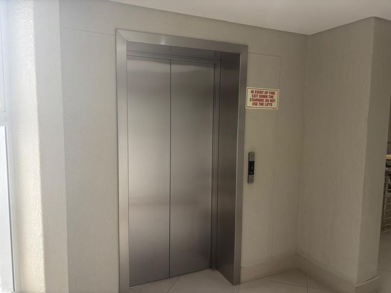 A clean and well-maintained office building hallway featuring a modern stainless steel elevator and clear fire safety signage.