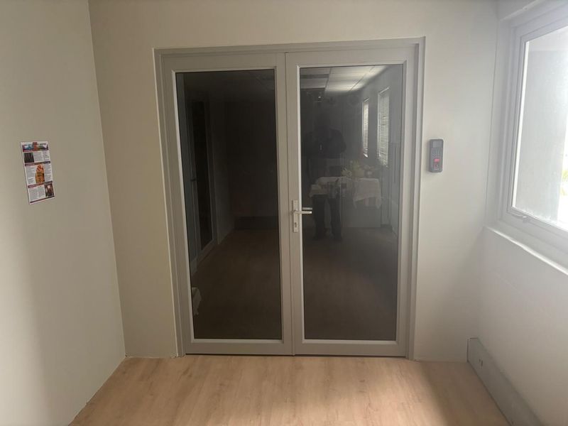A clean, modern office entry area featuring double glass doors with an electronic keypad access control system and light wood-look laminate flooring.