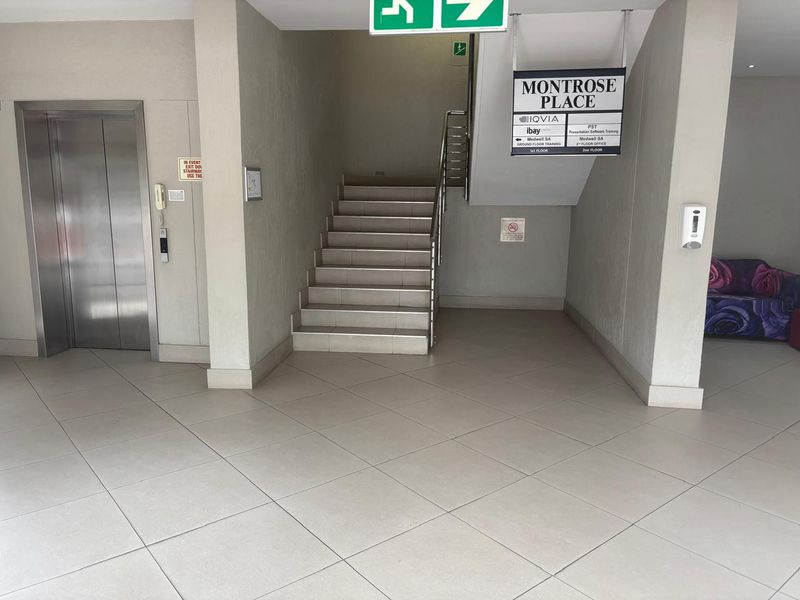 A clean and well-maintained office building lobby featuring a tiled floor, elevator access, and a central staircase with directory signage.