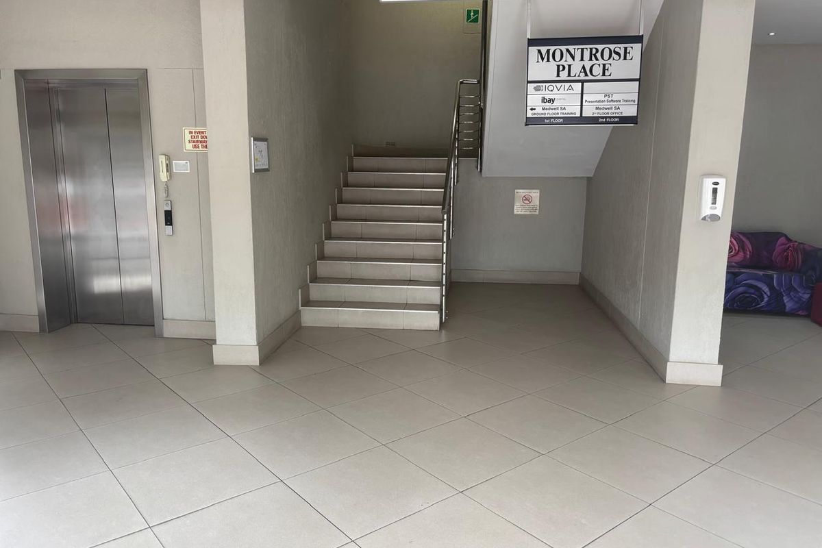 A clean and well-maintained office building lobby featuring a tiled floor, elevator access, and a central staircase with directory signage.