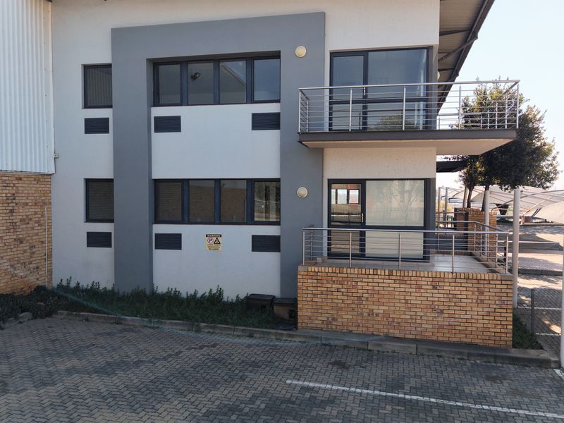 Modern industrial building facade featuring a combination of brick and rendered finishes, with a balcony, aluminium windows, and paved parking area.