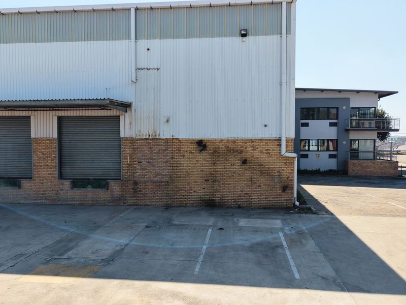 Rear view of an industrial warehouse featuring roller shutter doors, brick and metal cladding, and a paved loading or parking yard area.