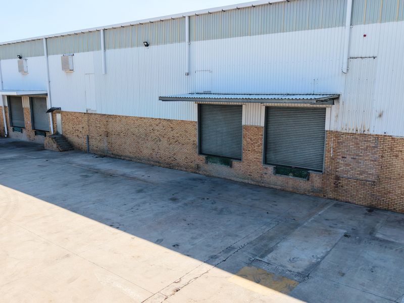 Industrial warehouse exterior featuring multiple roller shutter loading doors, a spacious concrete yard, and a combination of brick and metal cladding construction.