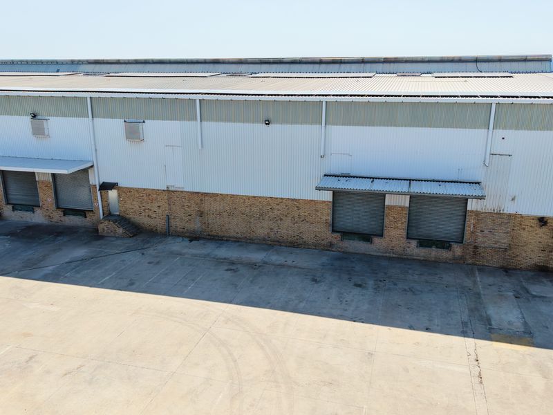 Aerial view of an industrial warehouse facility featuring multiple roller shutter doors, loading bay canopies, and a spacious concrete yard for logistics operations.