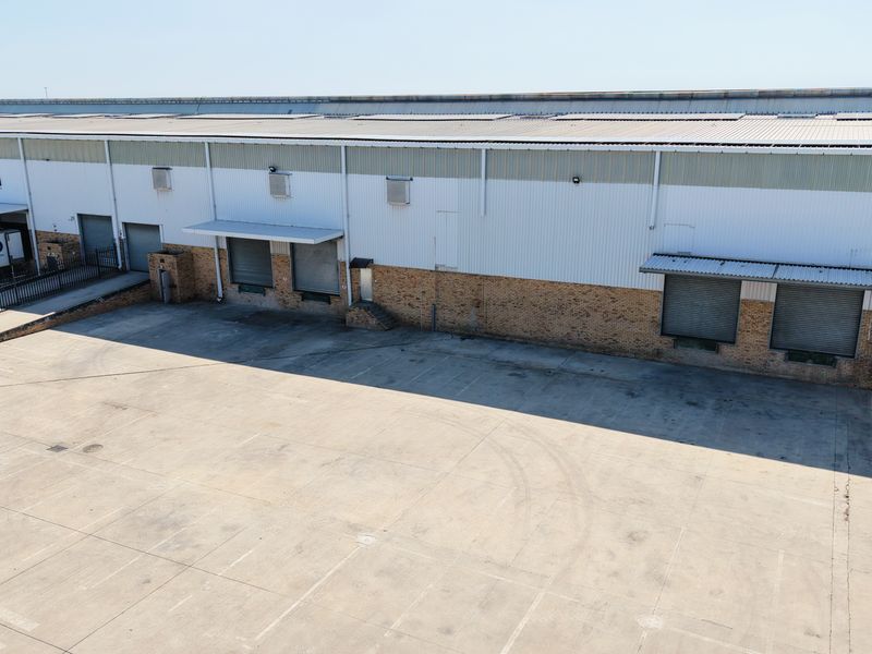 Aerial view of an industrial warehouse facility featuring multiple roller shutter loading bays, a large concrete yard, and durable brick and metal cladding construction.