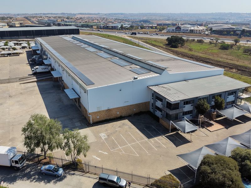 Aerial view of a large industrial warehouse facility featuring a metal roof with solar panels, paved parking, and dedicated loading bay areas.