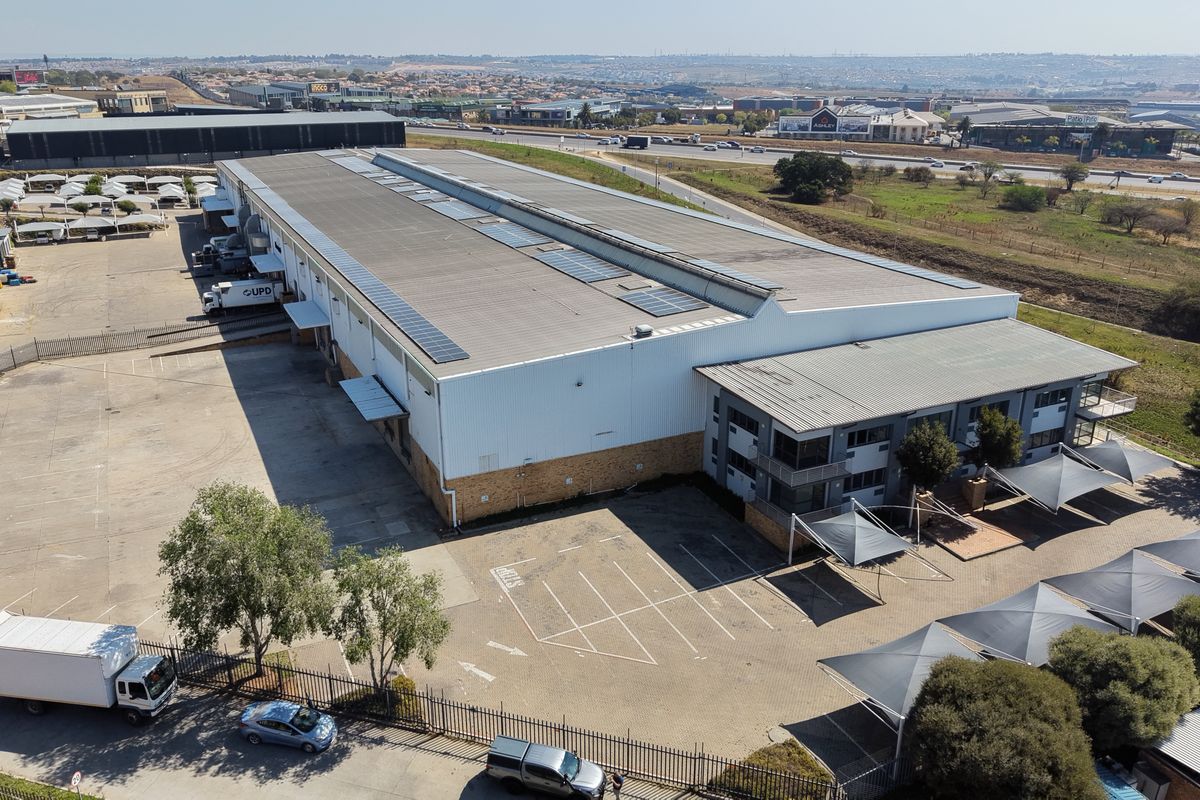 Aerial view of a large industrial warehouse facility featuring a metal roof with solar panels, paved parking, and dedicated loading bay areas.