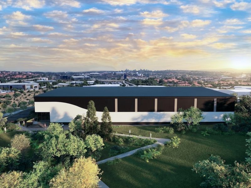 Aerial view of a modern industrial warehouse facility set within landscaped grounds, showcasing the building's exterior design and surrounding site layout.