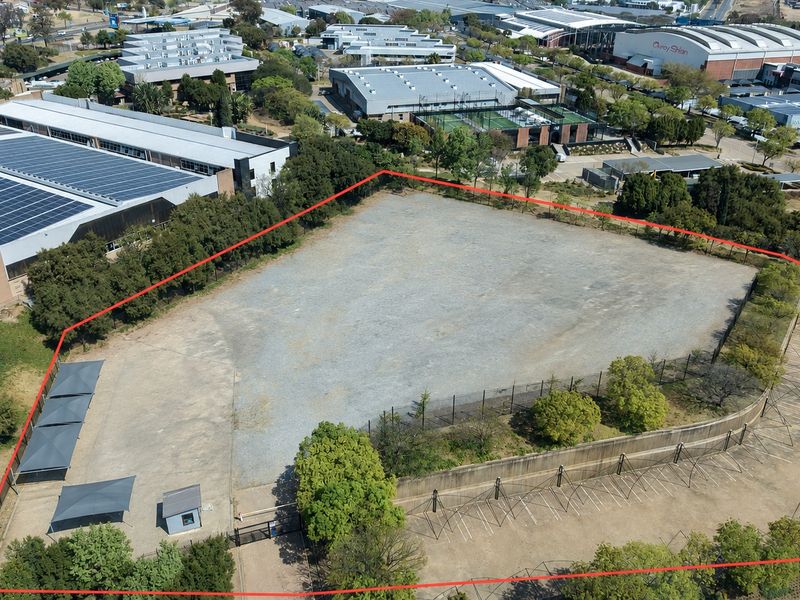 Aerial view of a large, level industrial land parcel featuring perimeter fencing, a retaining wall, paved parking bays with shade structures, and a security hut.