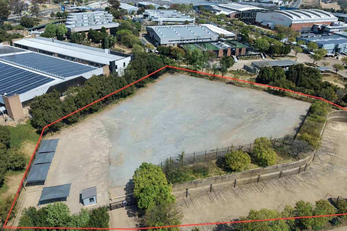 Aerial view of a large, level industrial land parcel featuring perimeter fencing, a retaining wall, paved parking bays with shade structures, and a security hut.