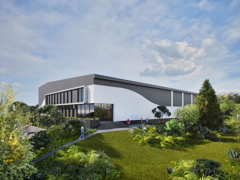 A modern industrial facility featuring a sleek metal-clad exterior, expansive glass frontage, and professionally landscaped surroundings.