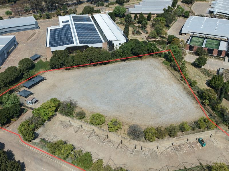 Aerial view of a vacant industrial plot featuring perimeter fencing, a paved parking area with shade structures, and established landscaping.