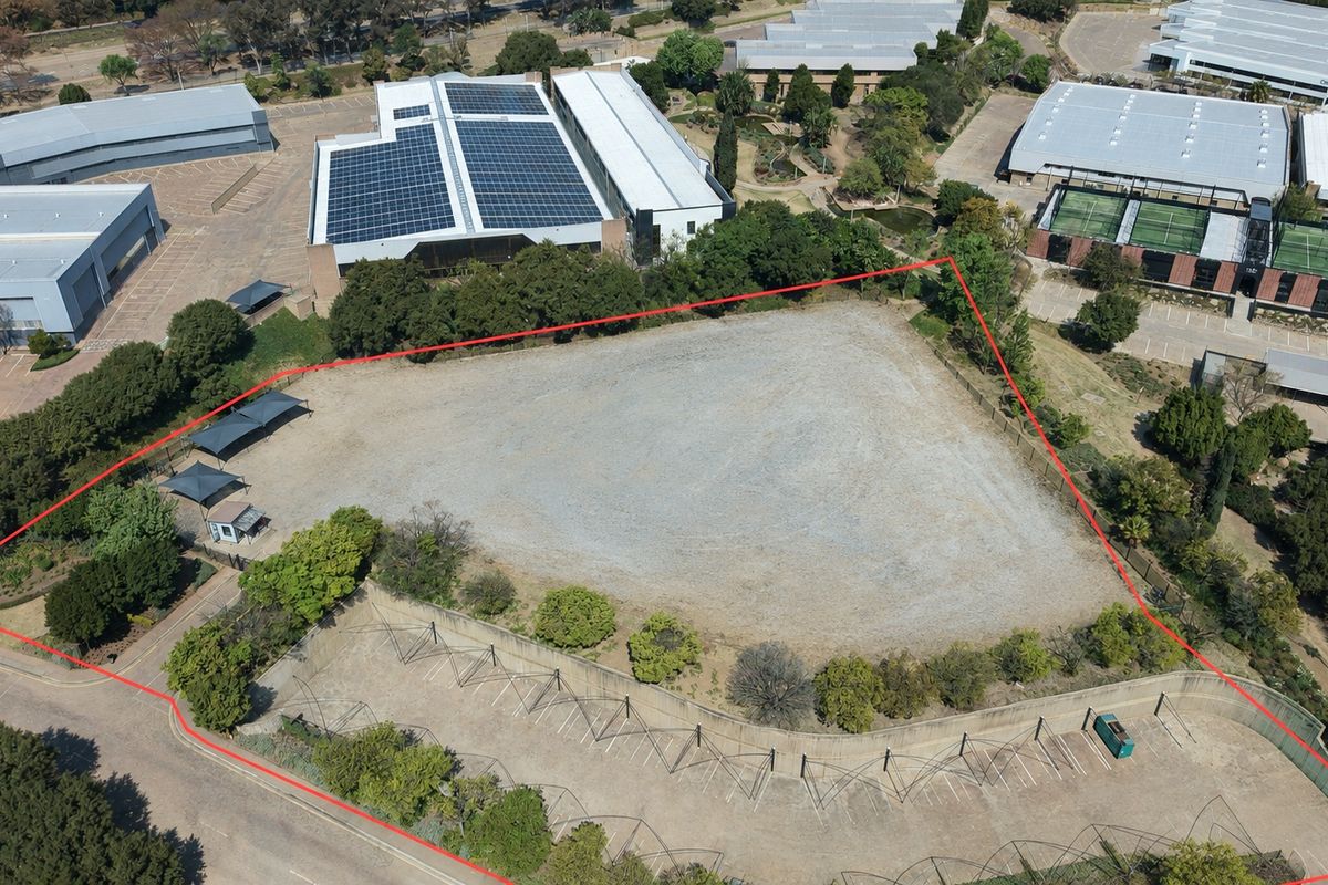 Aerial view of a vacant industrial plot featuring perimeter fencing, a paved parking area with shade structures, and established landscaping.