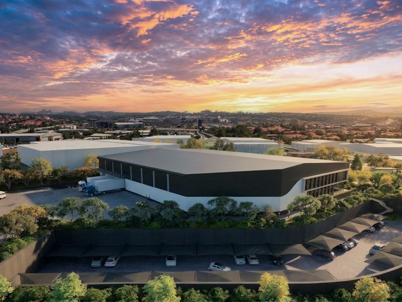 Aerial view of a modern industrial warehouse facility featuring a loading bay, extensive covered parking, and landscaped grounds at sunset.