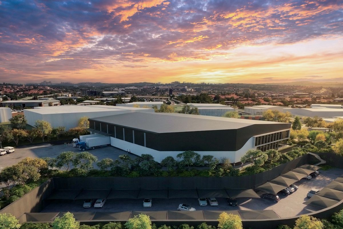 Aerial view of a modern industrial warehouse facility featuring a loading bay, extensive covered parking, and landscaped grounds at sunset.