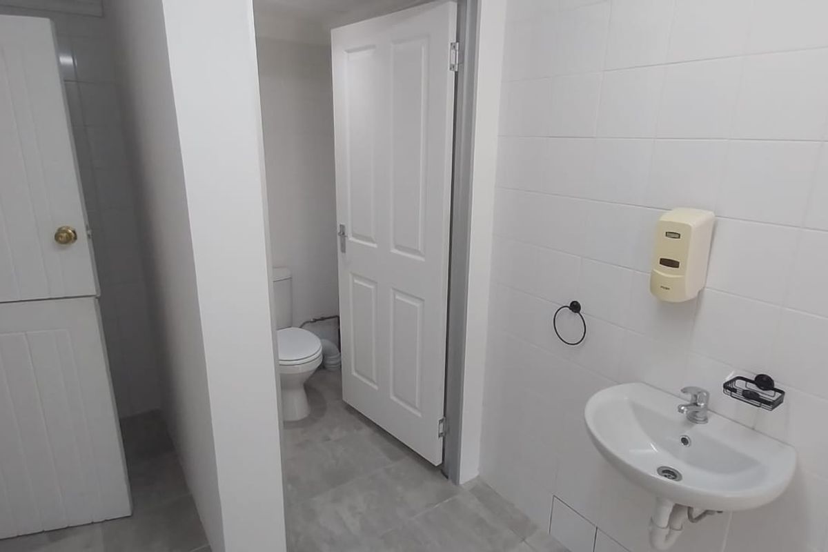A clean, functional office restroom featuring white wall tiles, a wall-mounted basin, and a separate toilet cubicle.