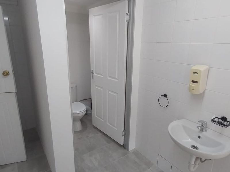 A clean, functional office restroom featuring white wall tiles, a wall-mounted basin, and a separate toilet cubicle.