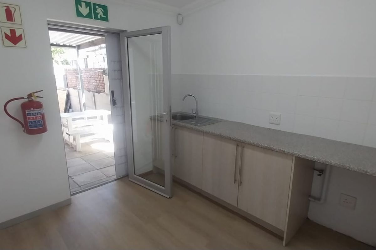 A functional office kitchenette featuring built-in cabinetry, a stainless steel sink, and direct access to an outdoor patio area.