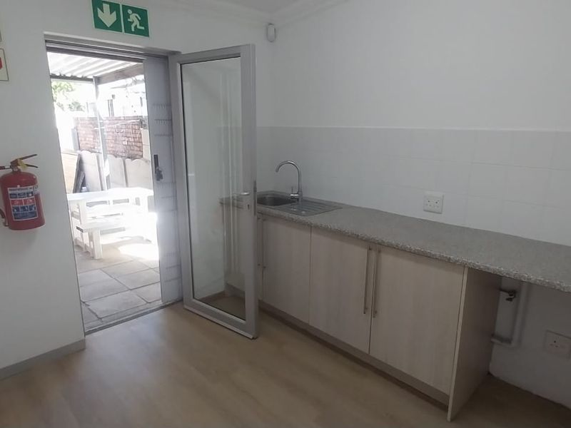 A functional office kitchenette featuring built-in cabinetry, a stainless steel sink, and direct access to an outdoor patio area.