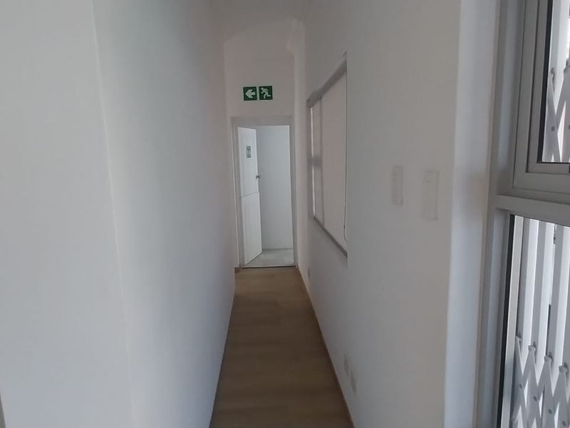 A clean, well-lit office hallway featuring laminate flooring, a security gate, and clear emergency exit signage.