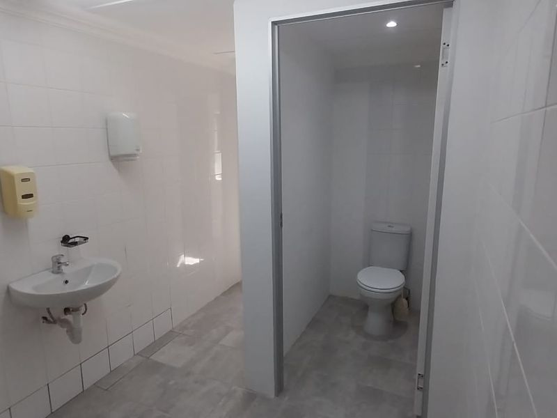 A clean, functional office bathroom featuring a wall-mounted basin, tiled walls, and a separate toilet cubicle with modern finishes.
