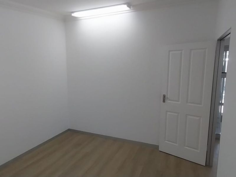 A clean, empty office space featuring neutral walls, laminate flooring, and a functional overhead light fixture.