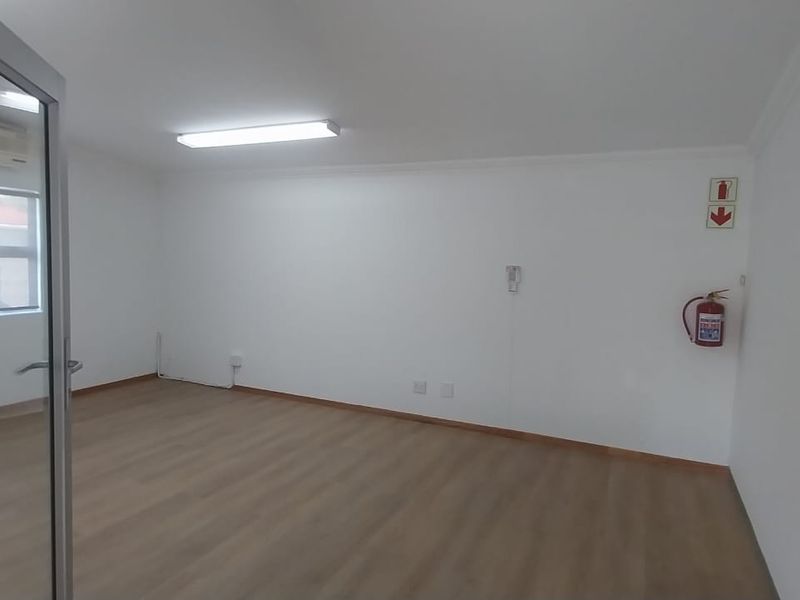 A clean, empty office space featuring laminate flooring, air conditioning, and bright overhead lighting, suitable for a professional workspace.