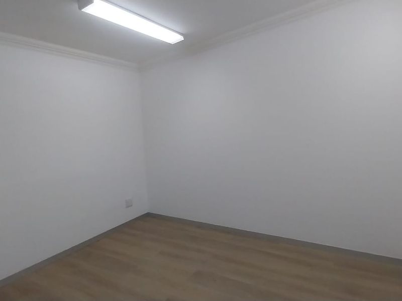A clean, empty office space featuring neutral white walls, laminate flooring, and a functional overhead light fixture.