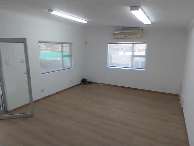 A bright, empty office space featuring laminate flooring, split-system air conditioning, and large windows with direct access to the exterior.