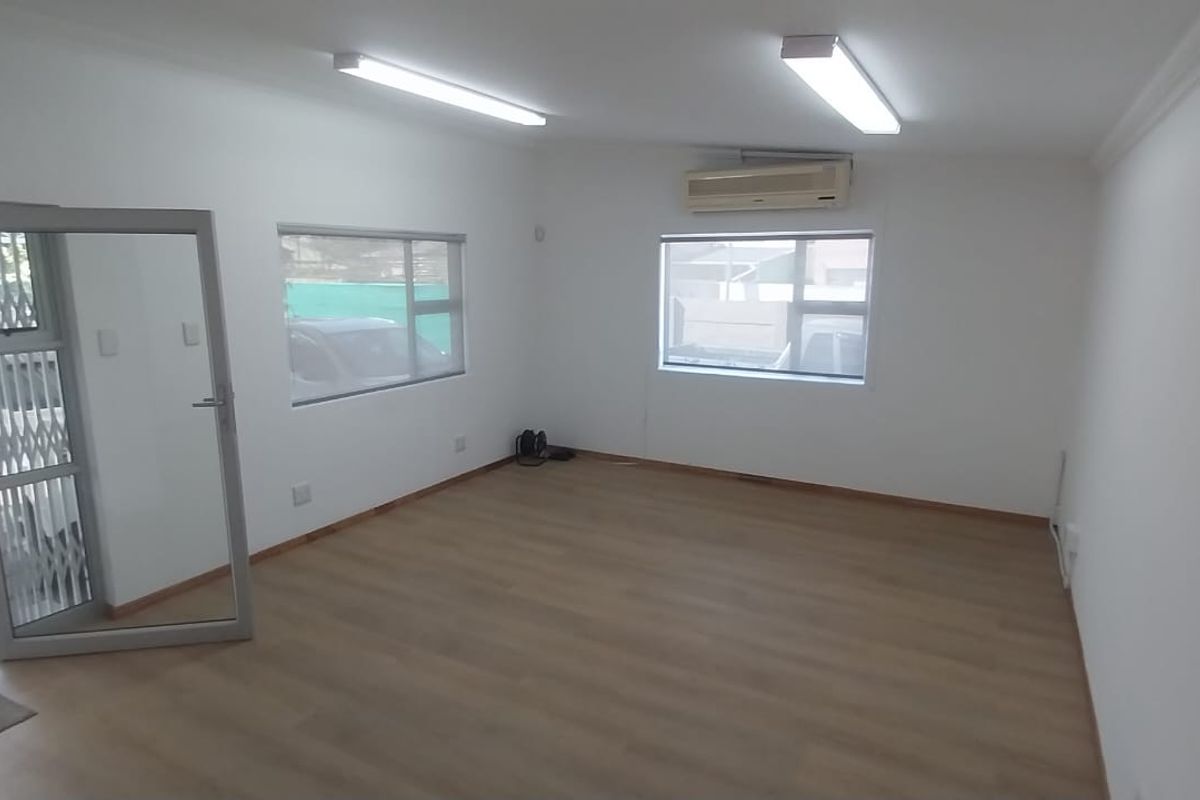 A bright, empty office space featuring laminate flooring, split-system air conditioning, and large windows with direct access to the exterior.