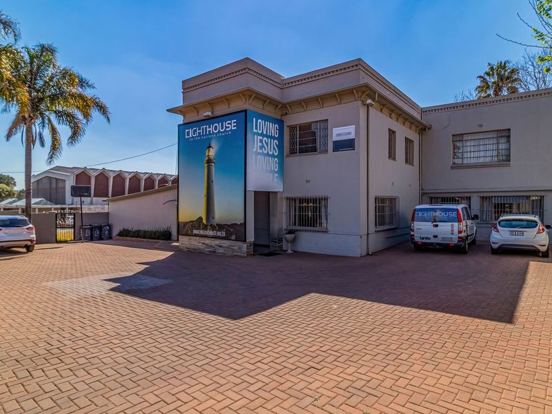 Front exterior view of a commercial property featuring a paved driveway, security window bars, and prominent building signage.