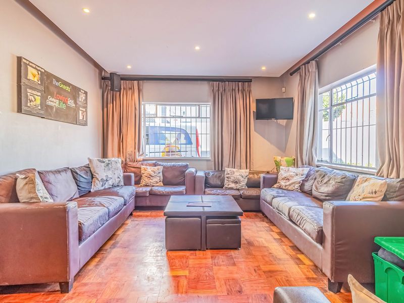 A living room featuring parquet flooring, recessed lighting, and windows fitted with security bars and curtain tracks.