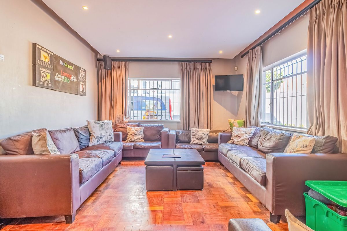 A living room featuring parquet flooring, recessed lighting, and windows fitted with security bars and curtain tracks.