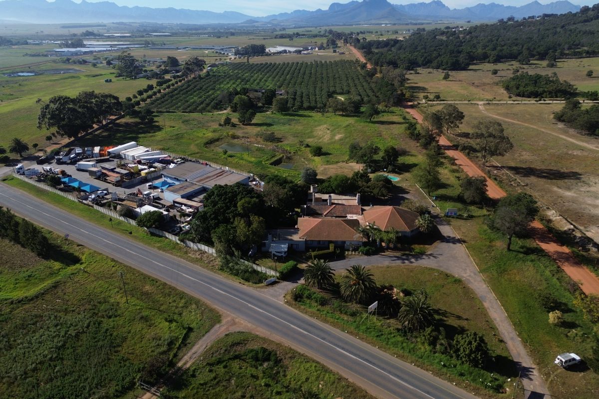 Aerial view of a farm property featuring a main residence, swimming pool, and adjacent commercial or storage yard area with mountain views.