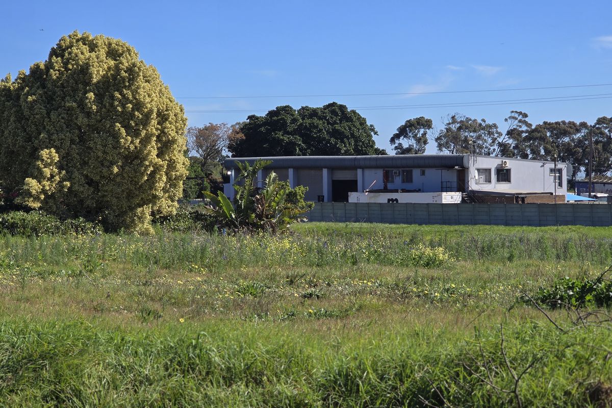 View of a large open field with a precast concrete boundary wall and an industrial shed structure in the background.