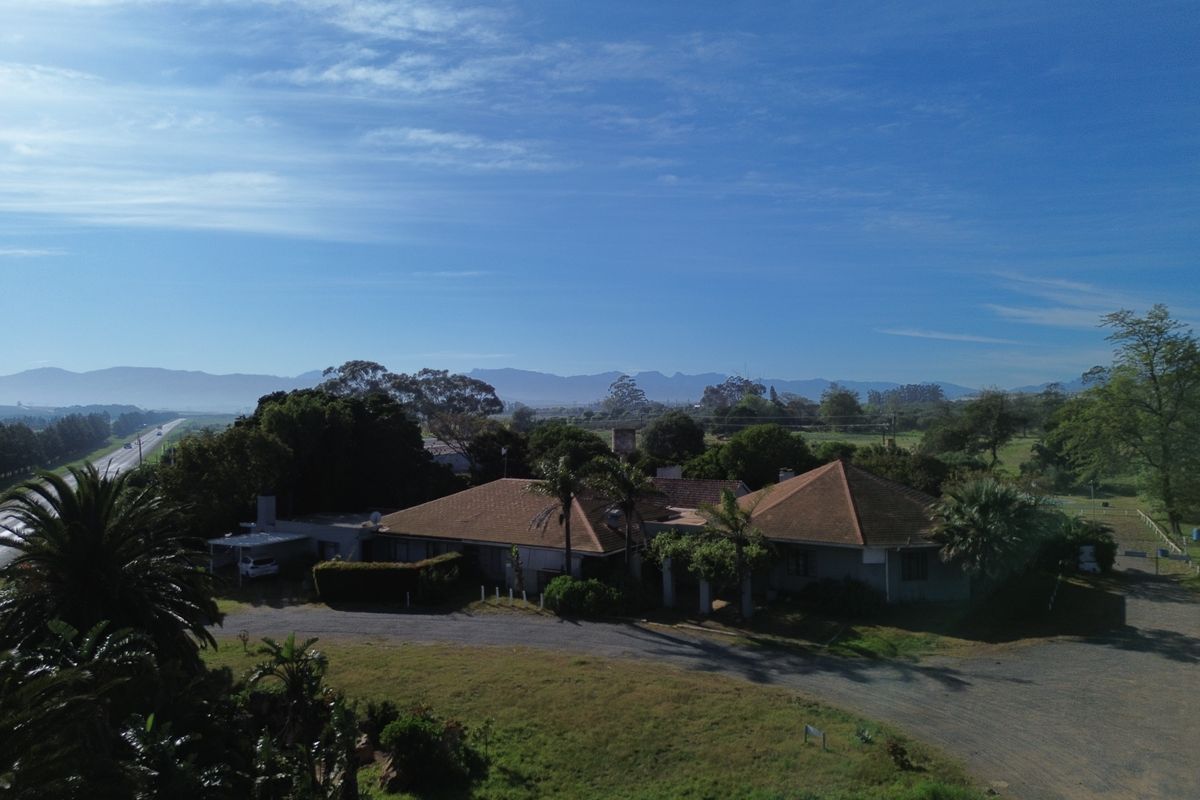 Aerial view of the farm property showcasing the main dwelling, surrounding grounds, gravel driveway, and expansive mountain landscape views.