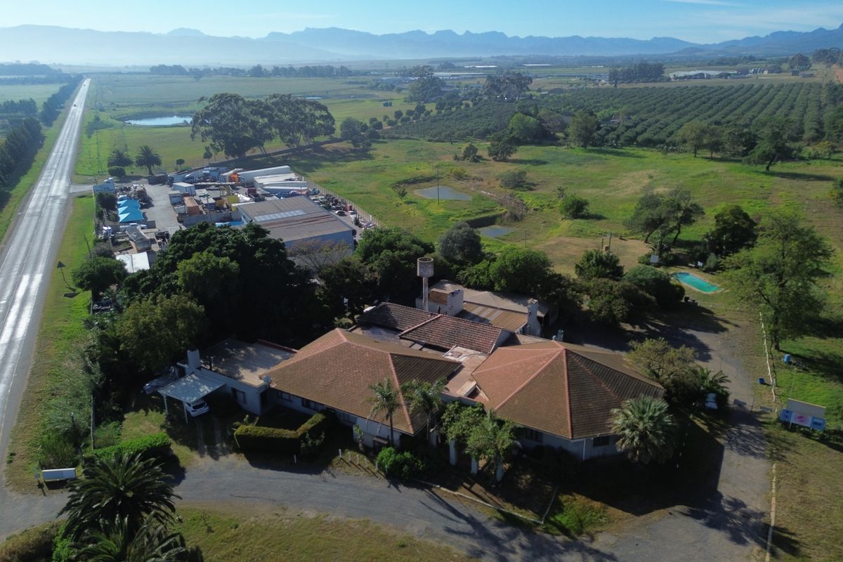 Aerial view of a farm property featuring a main residence with a tiled roof, swimming pool, and surrounding agricultural land.